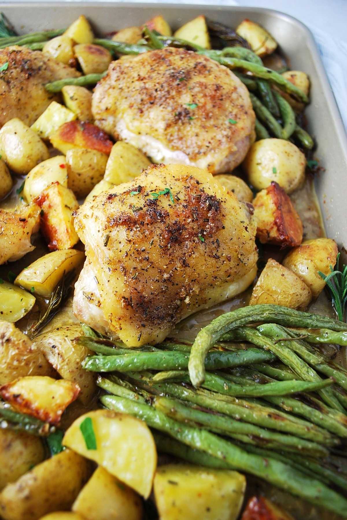 close up of roasted chicken with vegetables in a sheet pan sprinkled with chopped parsley