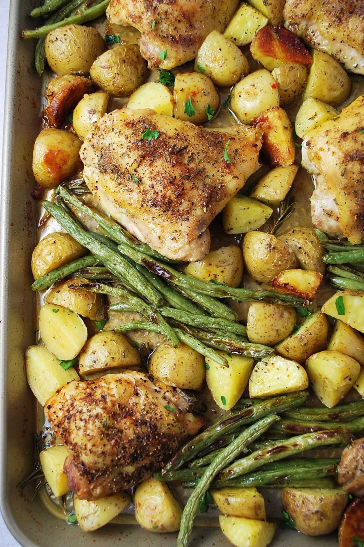 overhead photo of roasted chicken thighs, green beans, and potatoes in a pan