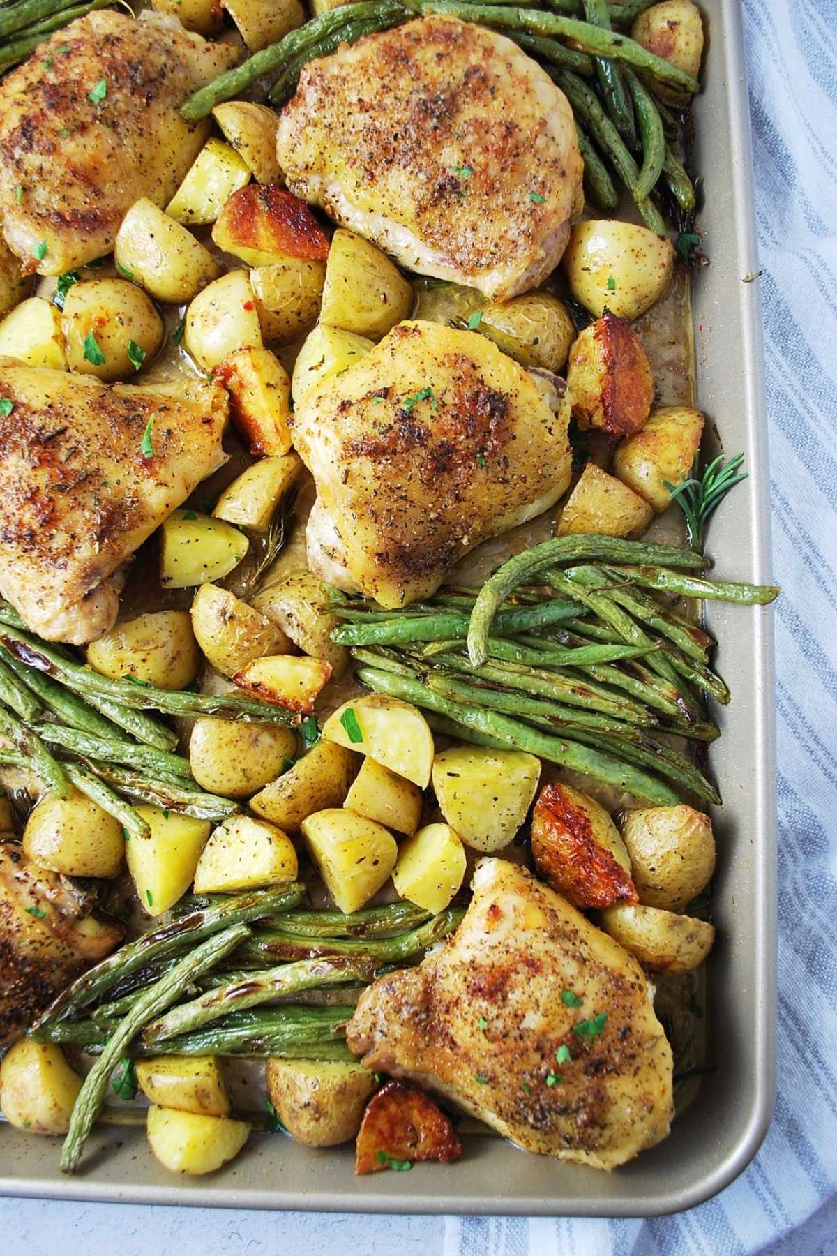 roasted chicken thighs with chopped Yukon gold potatoes and green beans in a large sheet pan with a napkin underneath