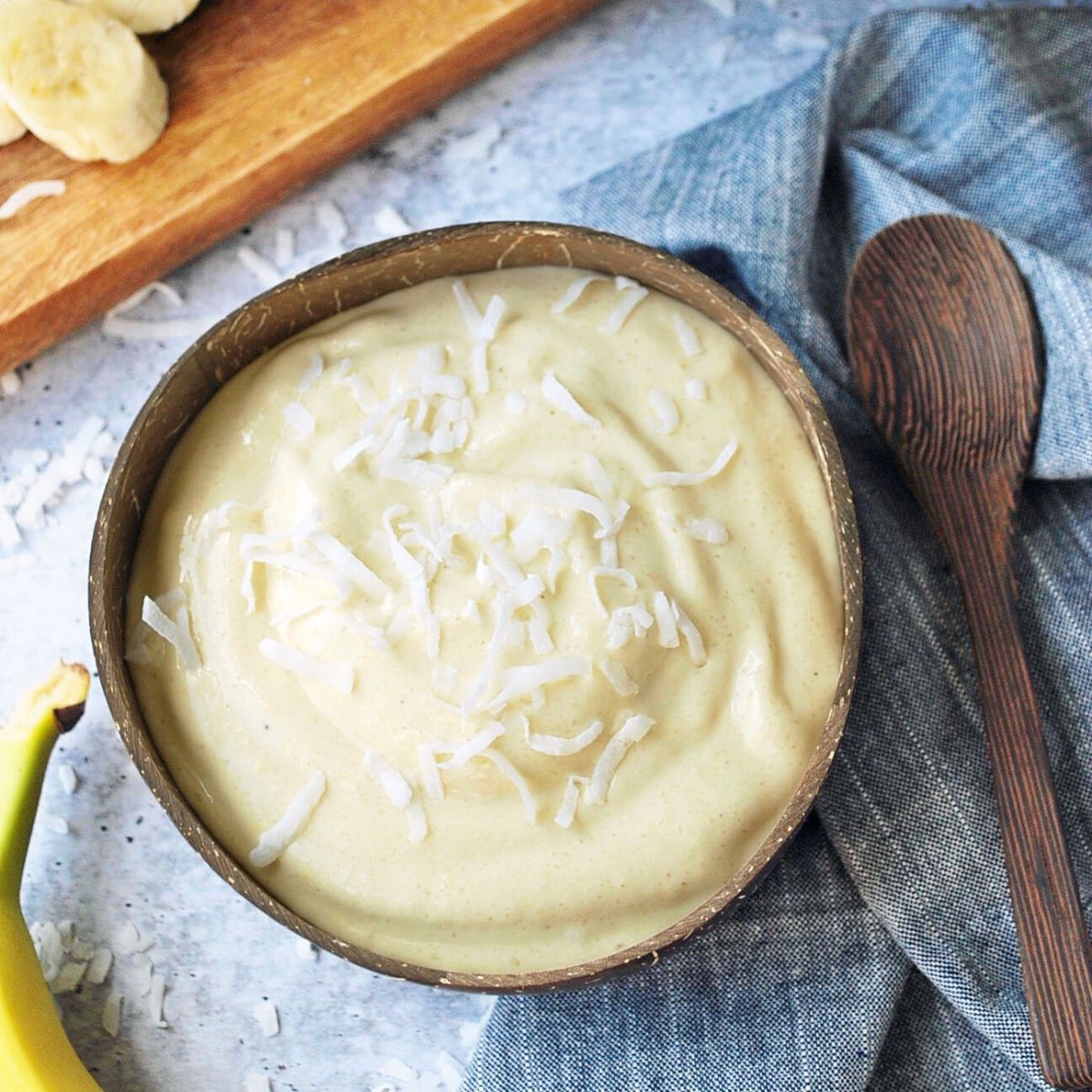 Tropical ice cream in a coconut bowl with banana and wooden spoon