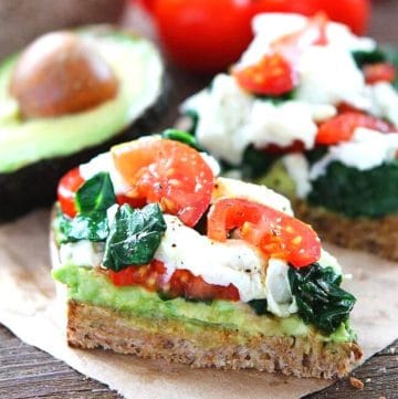 avocado toast topped with cheese, spinach and tomatoes on a piece of parchment paper