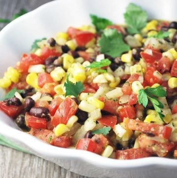 close up of a bowl of mojo salad with corn, black beans, tomatoes, fresh herbs, and dressing