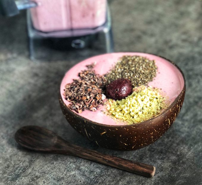 Cherry smoothie in a coconut bowl with chia seeds, cacao, hemp seeds and a frozen cherry on top