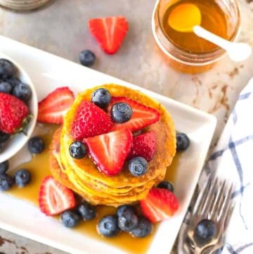 Gluten free coconut flour pancakes topped with strawberries, blueberries, and syrup