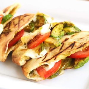 close up photo of 4 grilled pitas on a plate filled with tomato, mozzarella cheese, and avocado