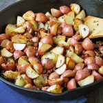garlic roasted potatoes in a cast iron skillet with a wooden spoon
