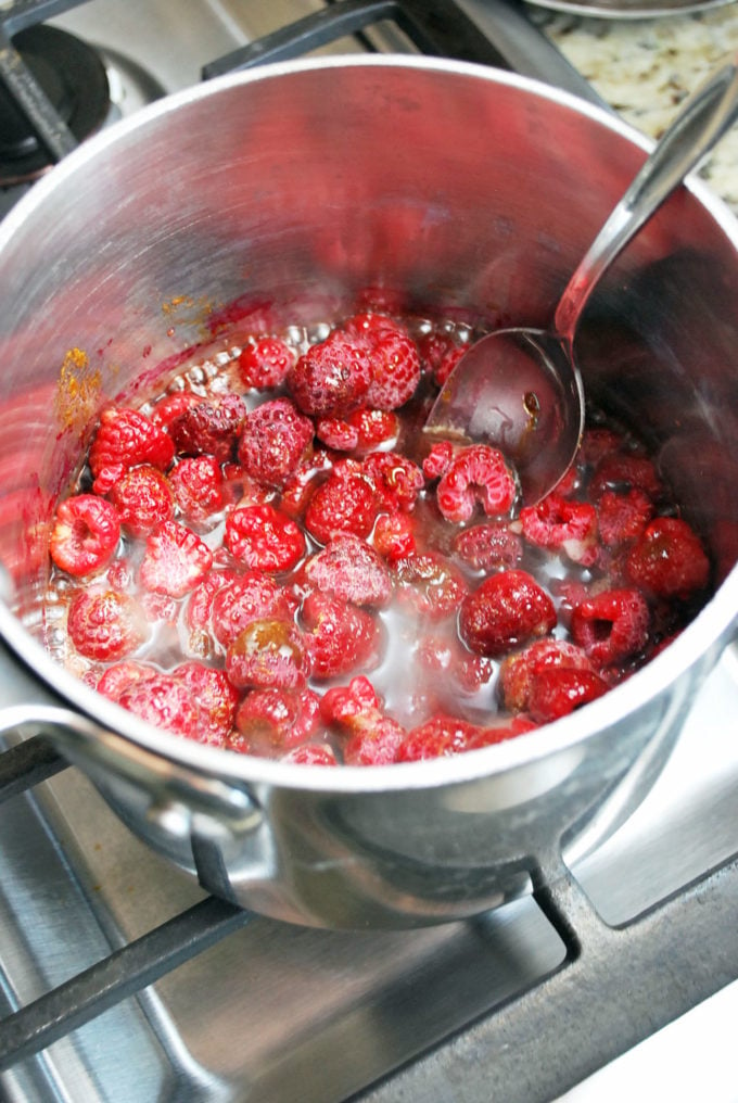 Raspberry compote cooking in a stainless steel pot with a spoon