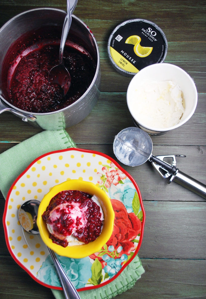 Overhead photo of cooked raspberry compote in a pot with lemon frozen mousse container, ice cream server and bowl of mousse topped with compote.