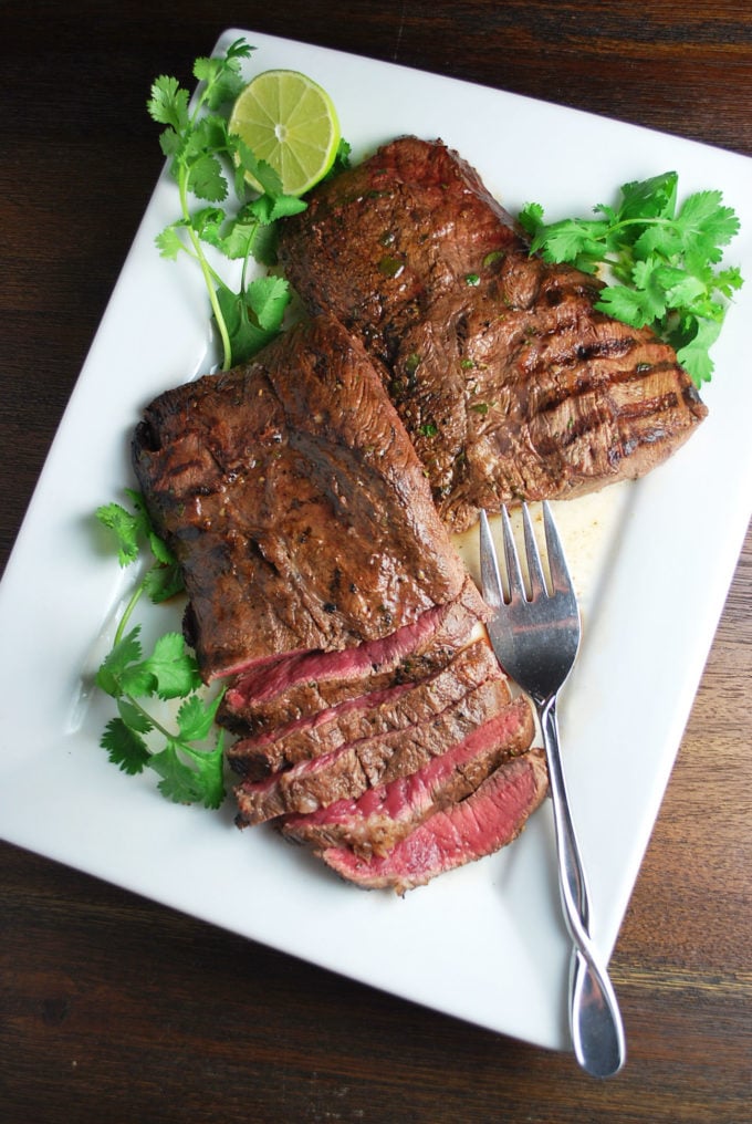 overhead photo of sliced flat iron steak on a white platter with herbs