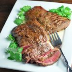 Sliced flat iron steak on a plate with fresh herbs