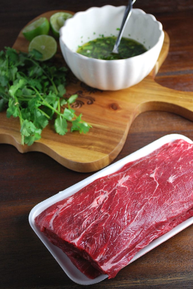 Uncooked flat iron steak with herbs and a bowl of marinade