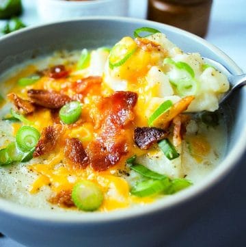 bowl of potato leek soup topped with shredded cheese, bacon, and green onions