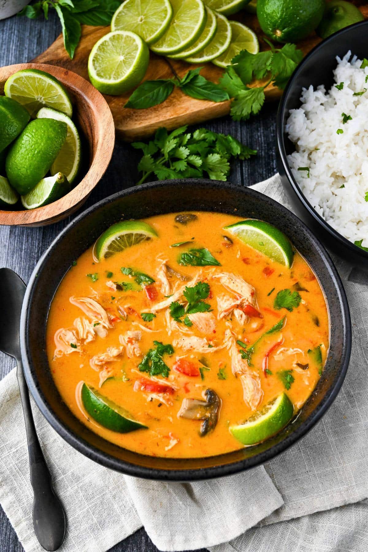 looking down at a bowl of soup with rice and fresh limes