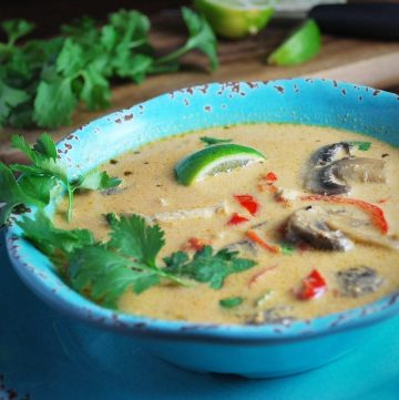 chicken curry soup with fresh lime, peppers, and mushrooms in a blue bowl garnished with fresh herbs