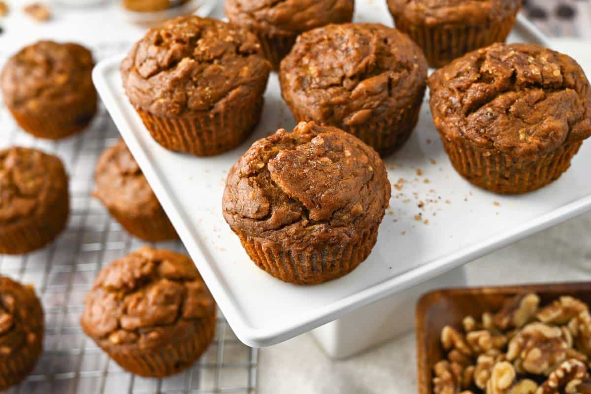 a tray of baked muffins with a rack of muffins next to it and a bowl of walnuts
