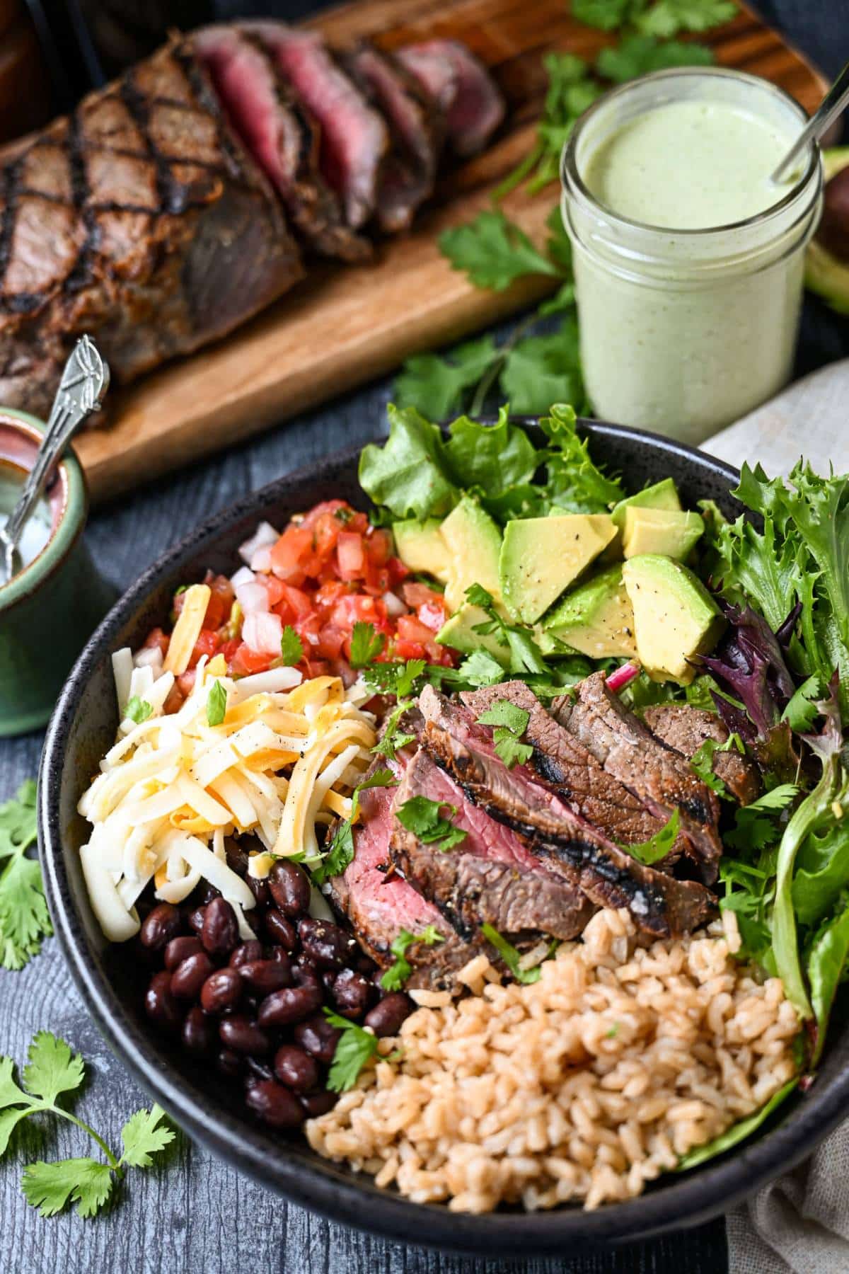 overhead photo of a grilled steak rice bowl with a jar of creamy cilantro lime dressing and sliced steak