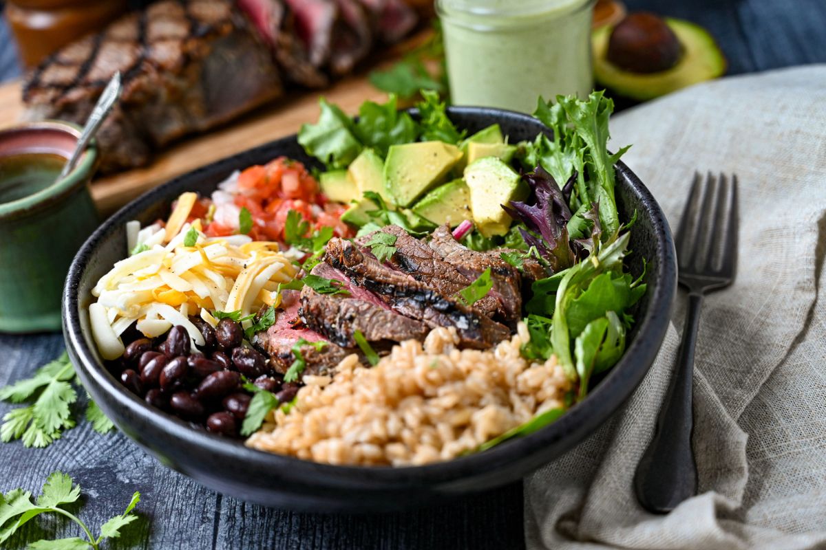 side view photo of a grilled steak bowl with rice, avocado and veggies