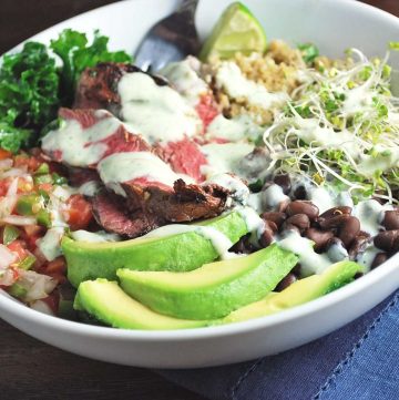 sliced avocado, steak, salsa, kale, black beans, quinoa, and bean sprouts in a bowl with a sauce