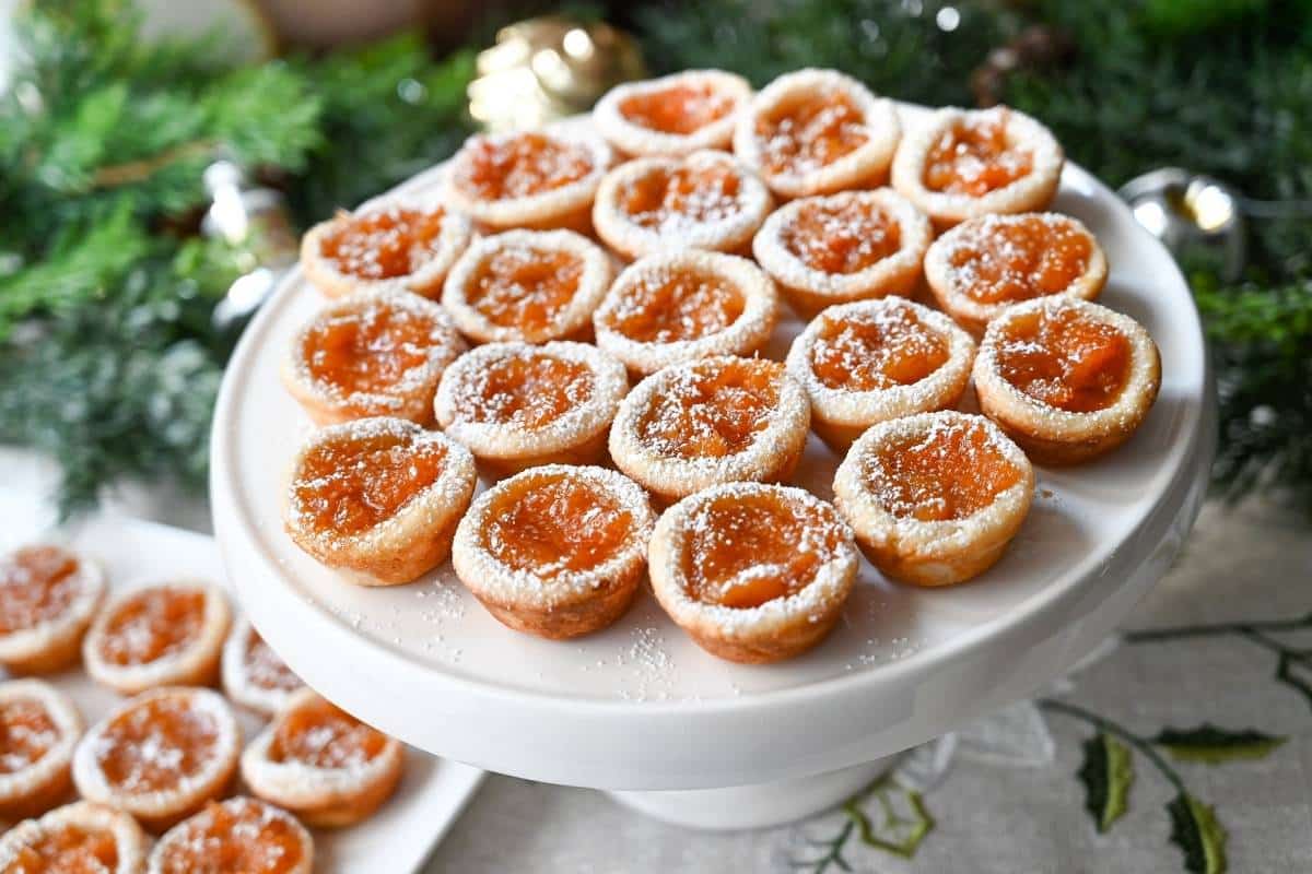 a  platter full of apricot tarts sprinkled with powdered sugar with a holiday background