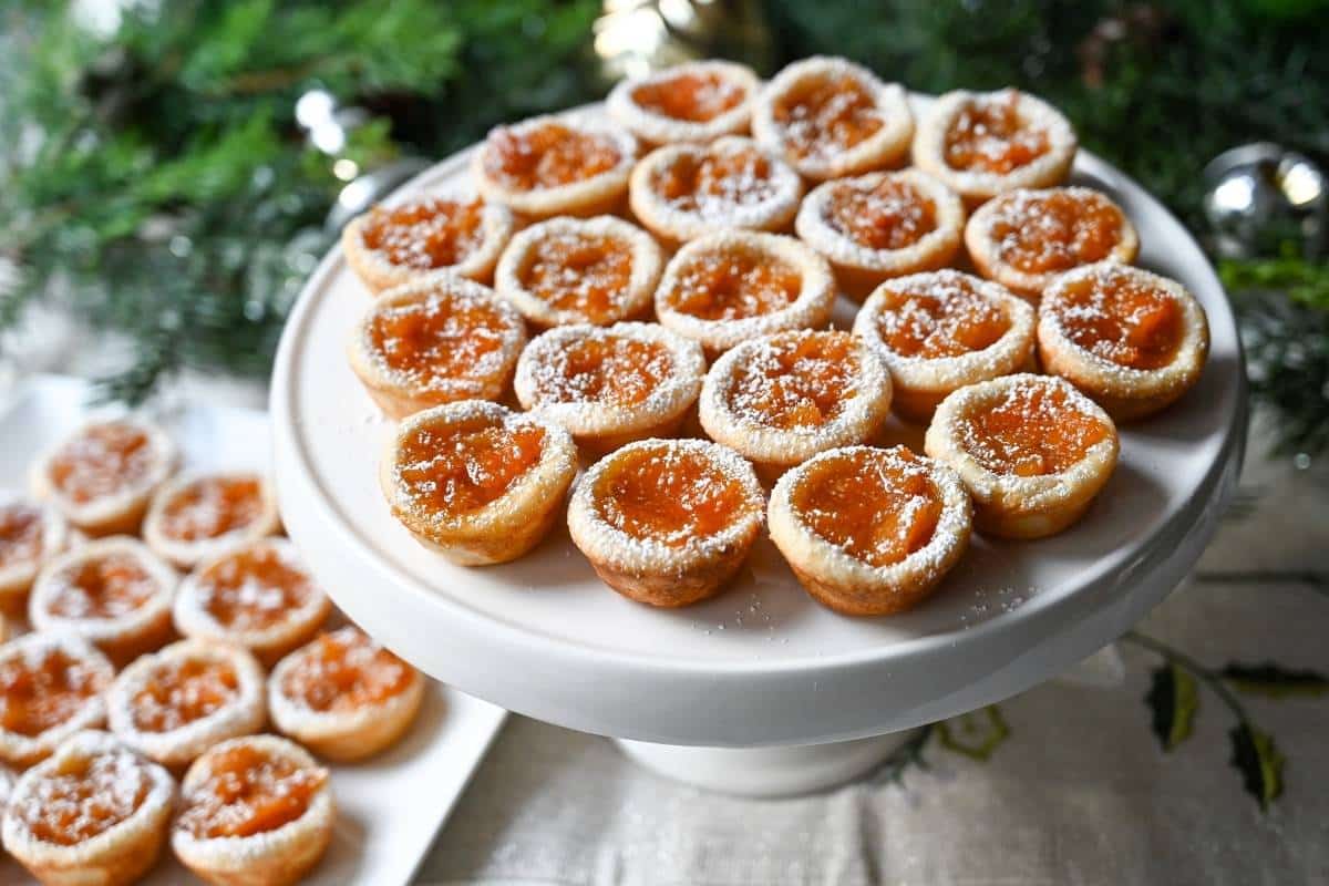 a platter of apricot tarts with greenery behind it