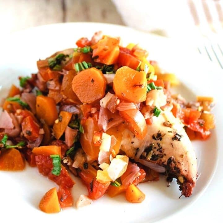 chicken breast topped with carrots and tomatoes with an herb garnish