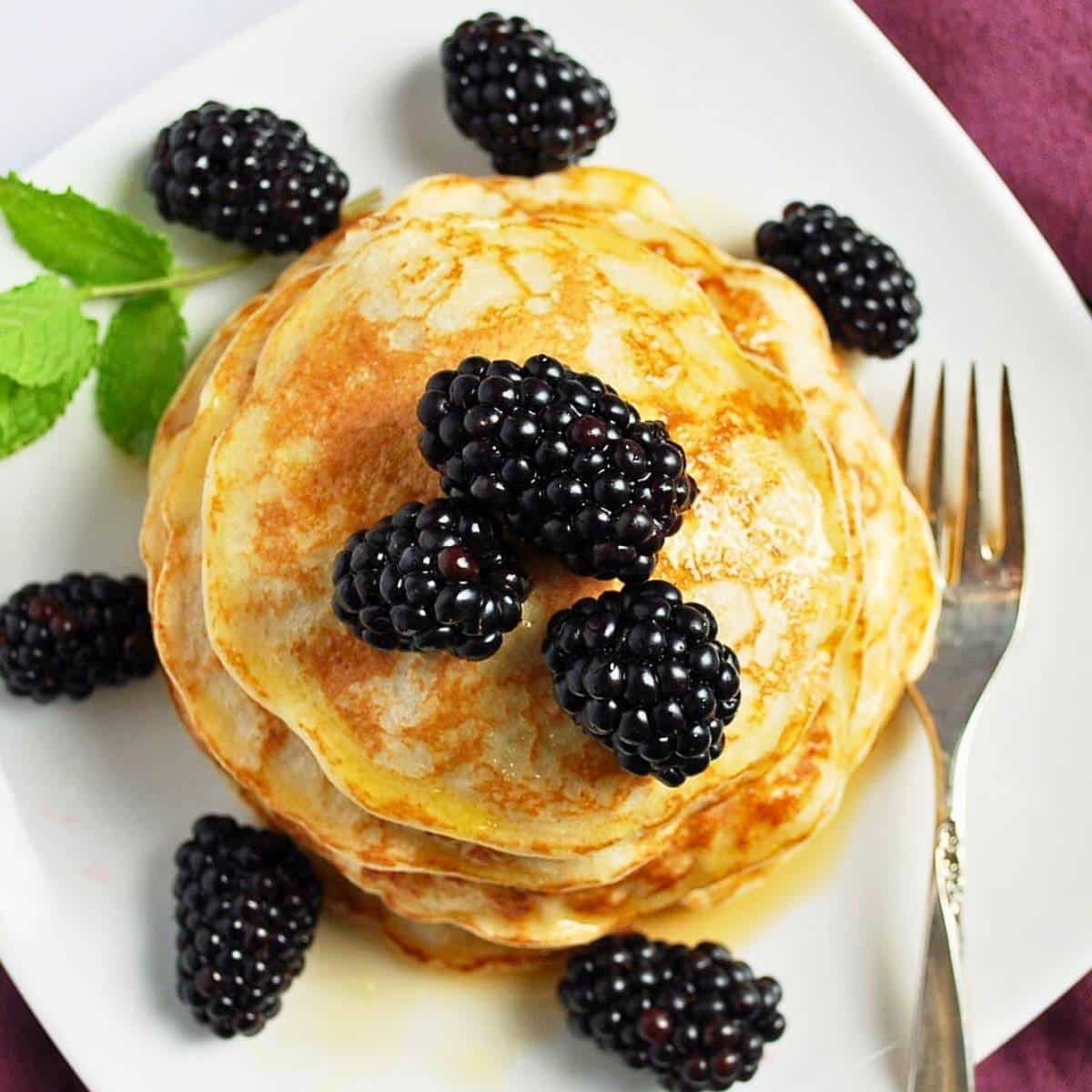 looking down at pancakes with syrup, berries and a fork on a plate