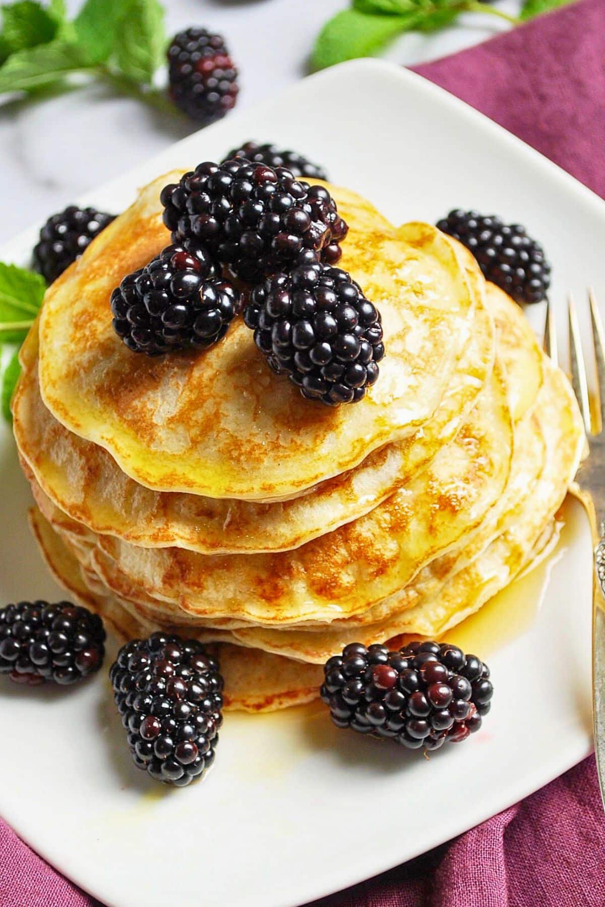 a tall stack of crepe like cottage cheese pancakes with blackberries and syrup