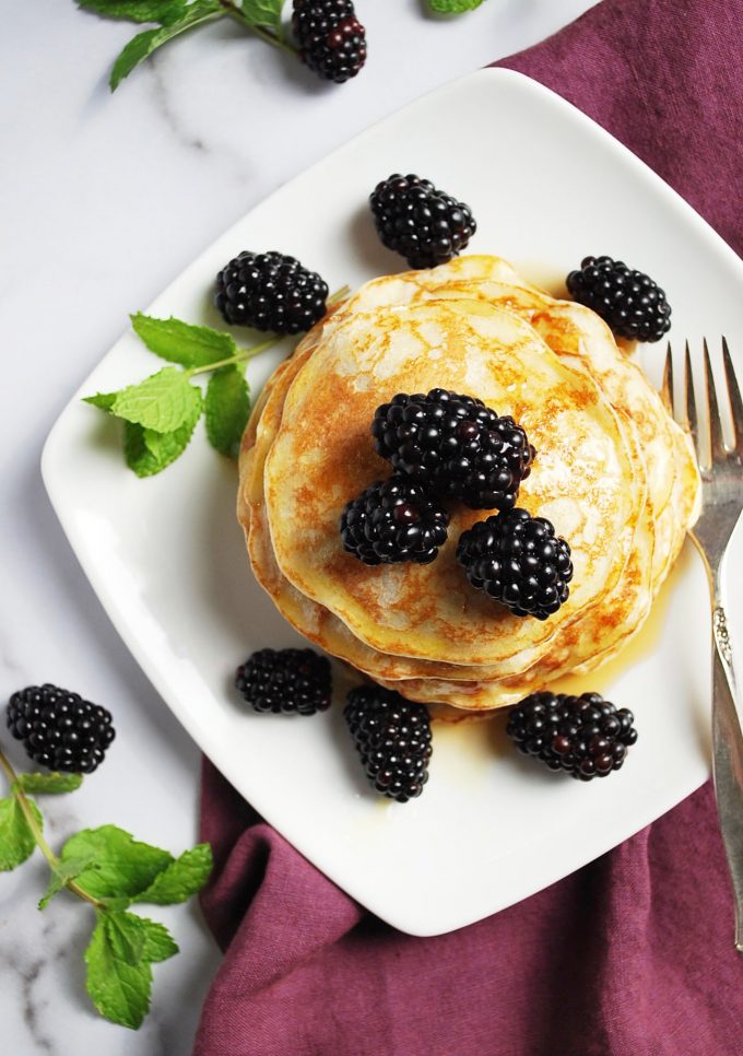 plate of pancakes with berries and syrup with fork and napkin