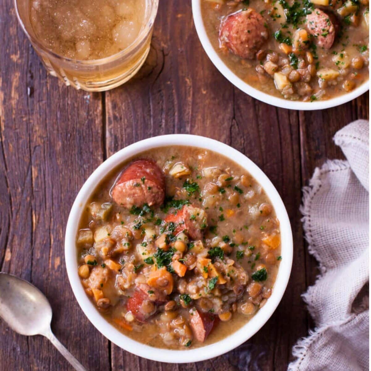 sausage lentil soup in two bowls with a drink