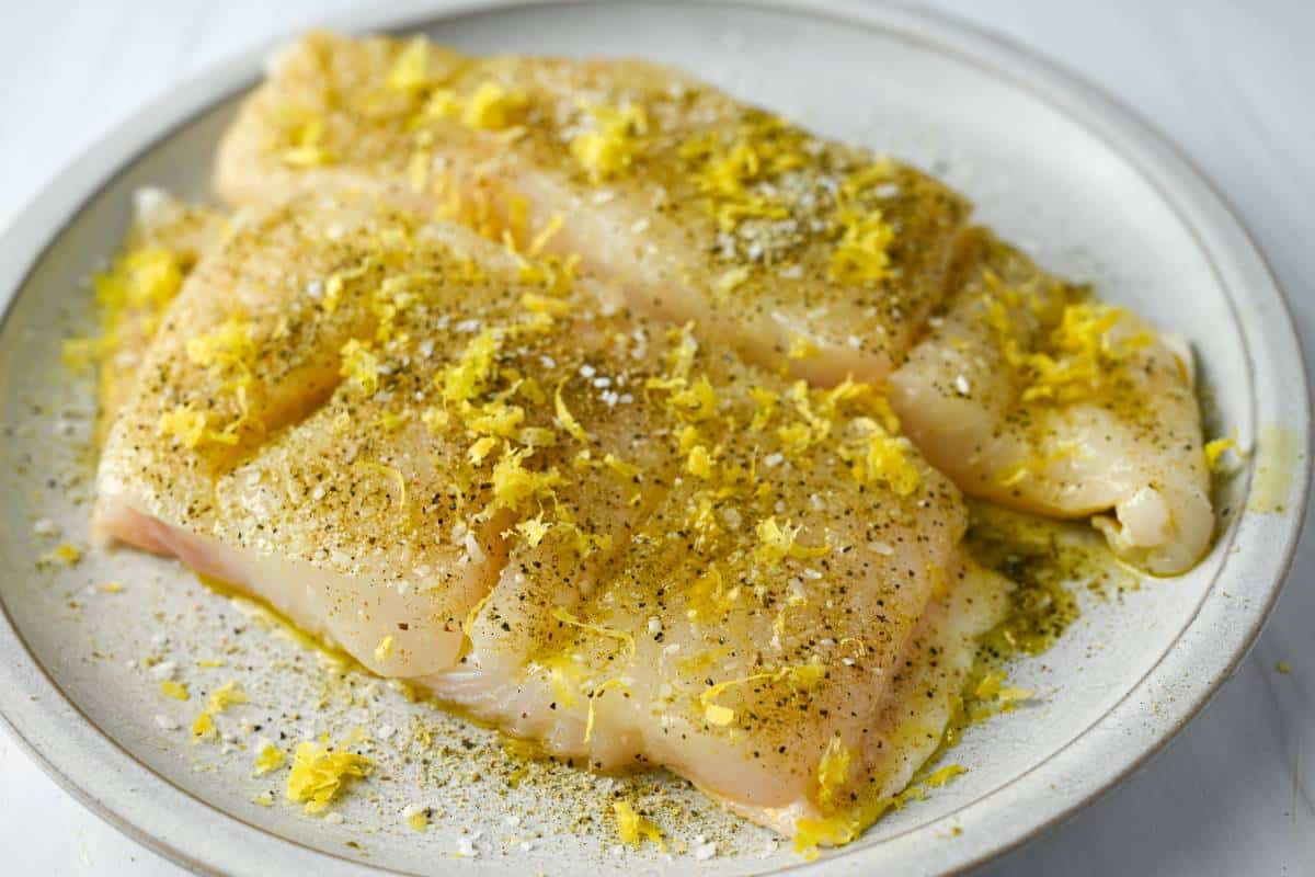 two halibut fillets on a plate with greek seasoning and fresh lemon zest
