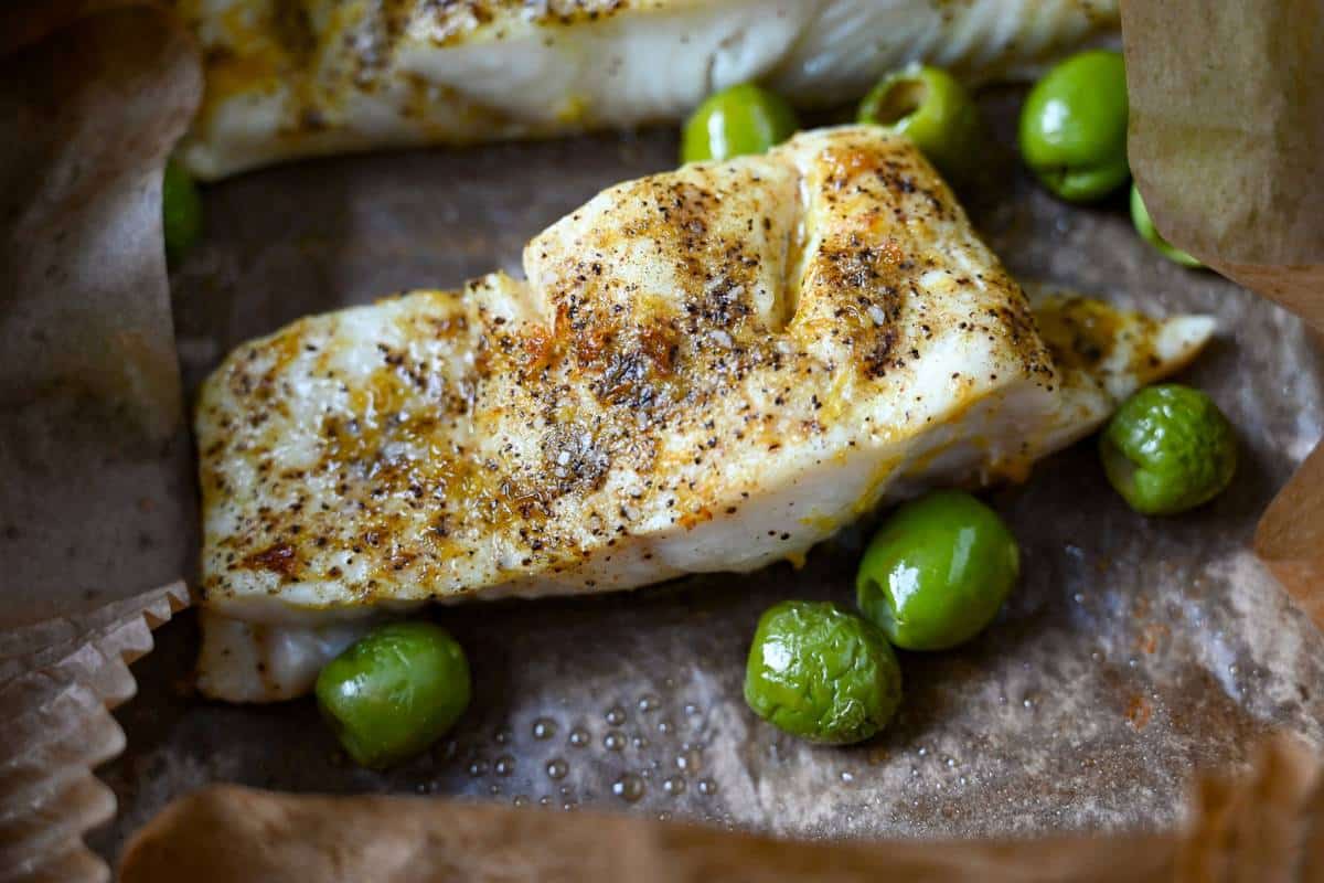 cooked halibut with olives in an air fryer basket with a parchment liner