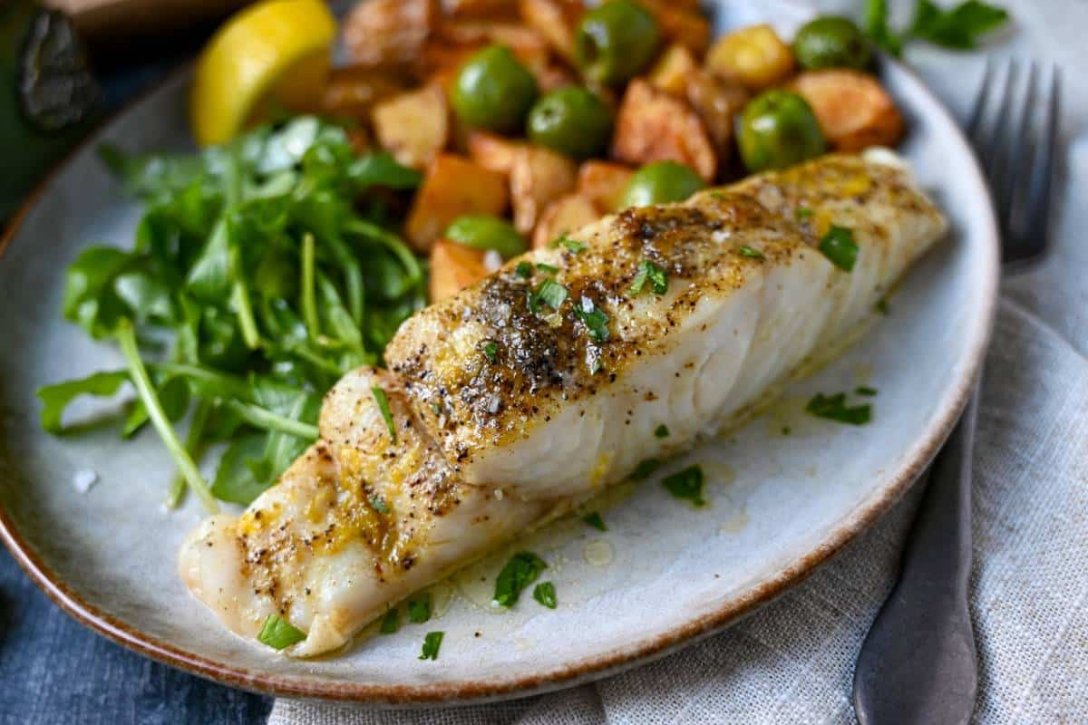 plated air fryer halibut with fresh lemon zest, arugula, and potatoes and olives on a plate