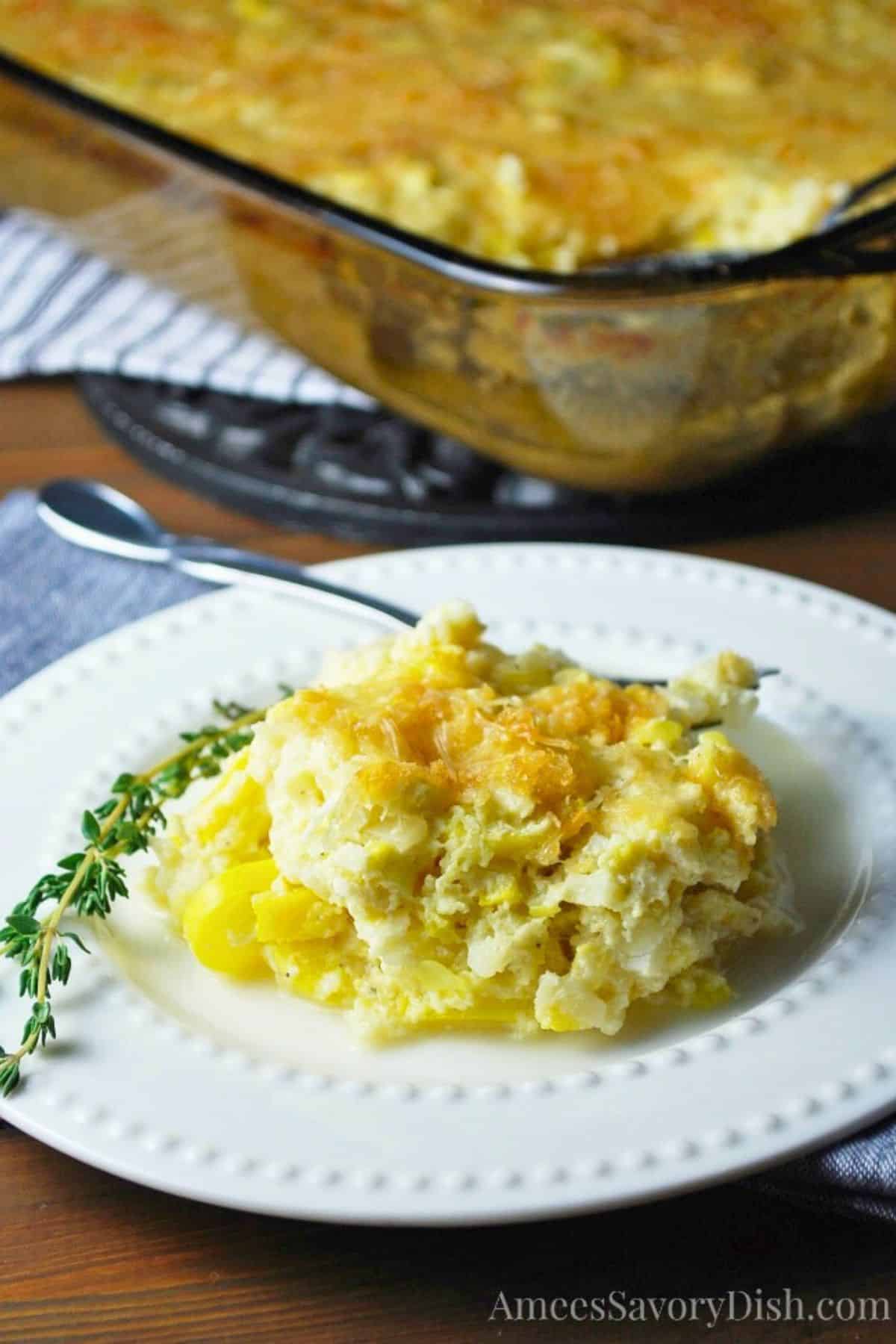 cauliflower squash casserole on a plate with a sprig of thyme and a casserole dish behind it