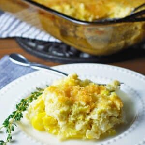 squash casserole on a plate with herbs with a pan of casserole behind it