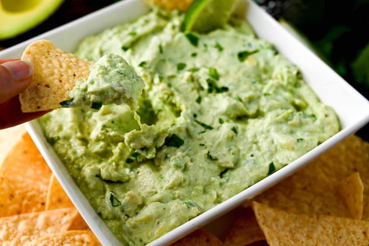 a chip dipping into a bowl of avocado dip on a platter of chips