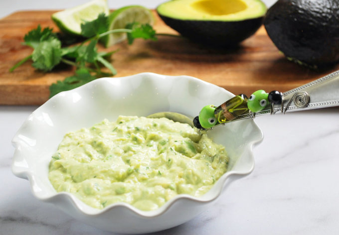 avocado dip in a white bowl with a spoon and avocado in the background