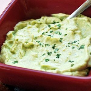 avocado dip in a red bowl topped with fresh herbs