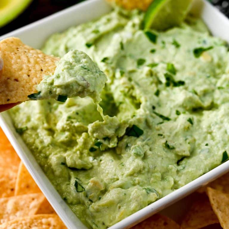 close up of a tortilla chip dipped into a bowl of avocado yogurt dip