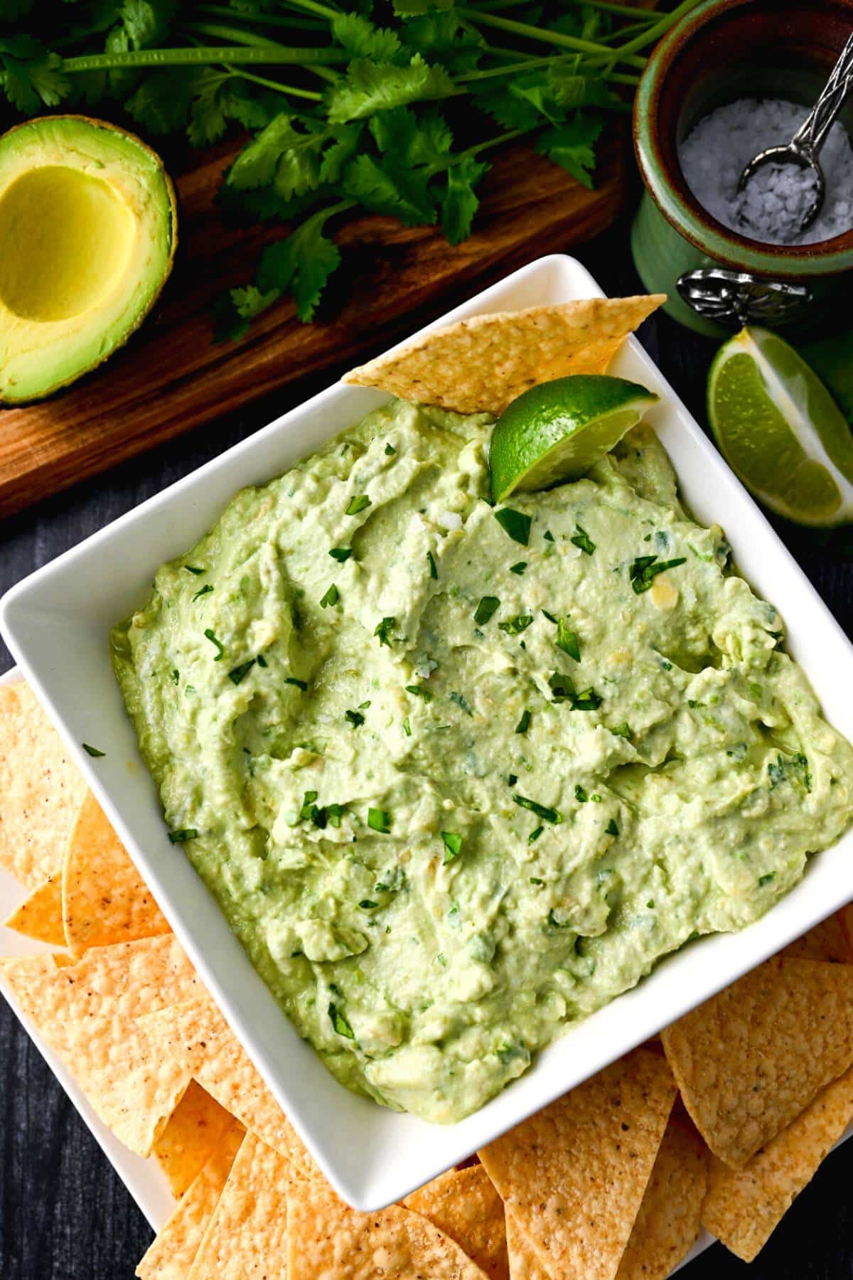 overhead photo of a bowl of avocado yogurt dip with chips, and fresh lime
