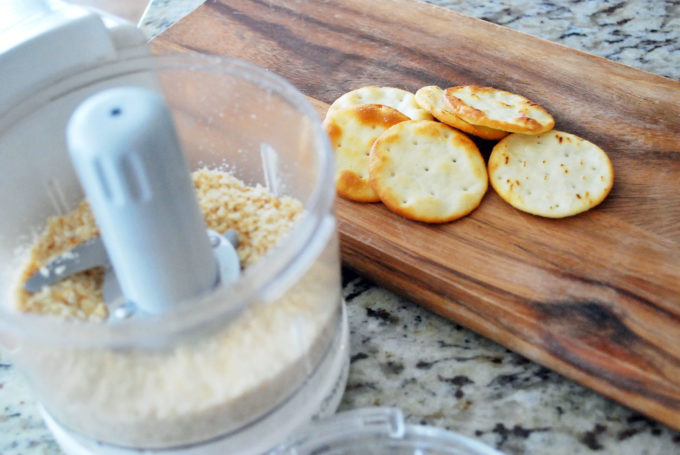 mini food processor with ground crackers with whole crackers in the background on a wood board