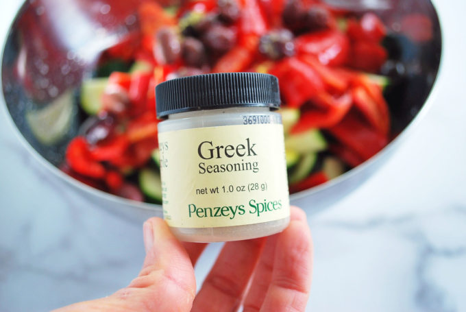 Jar of Greek seasoning with a bowl of vegetables in the background