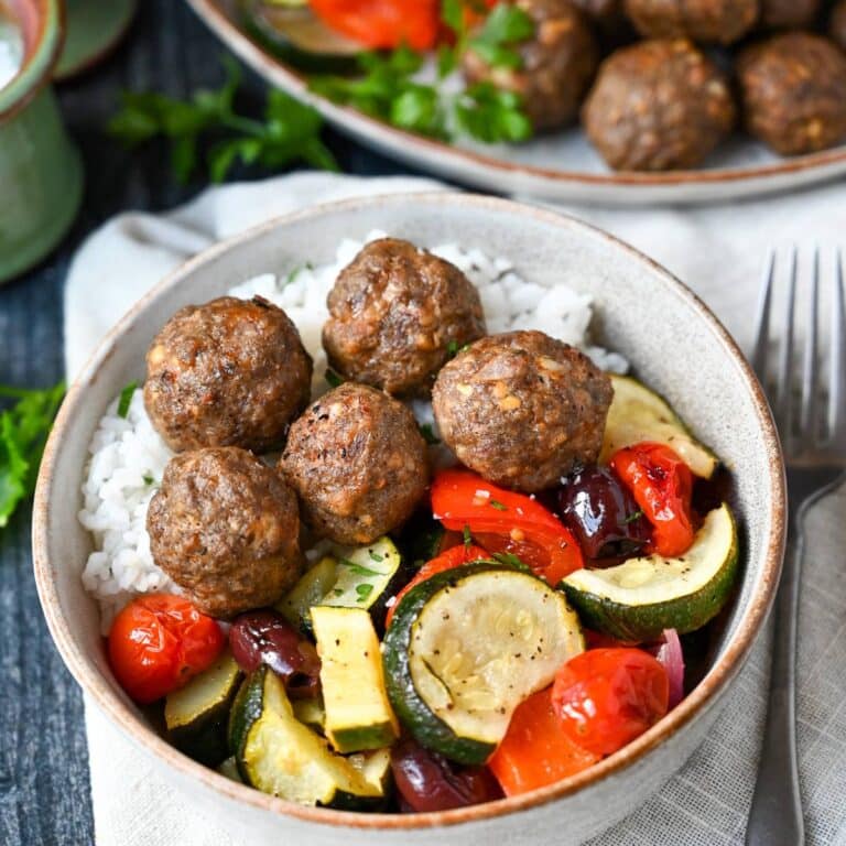 a bowl of meatballs with rice and roasted Greek vegetables with a fork and napkin