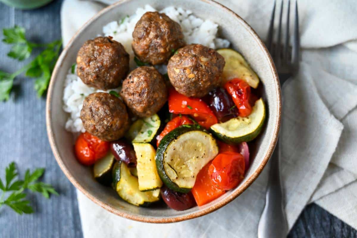 a bowl of jasmine rice with four meatballs and roasted mediterranean vegetables