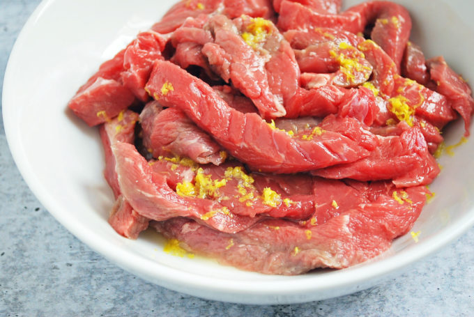 marinated sliced raw steak strips on a plate with lemon zest