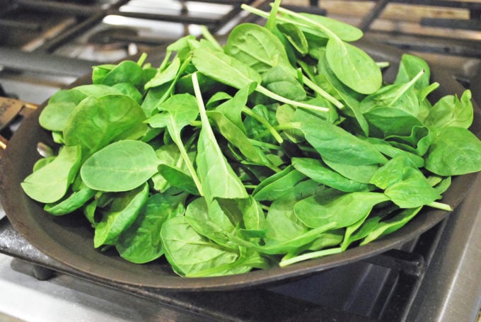 A close up of raw spinach leaves in a skillet