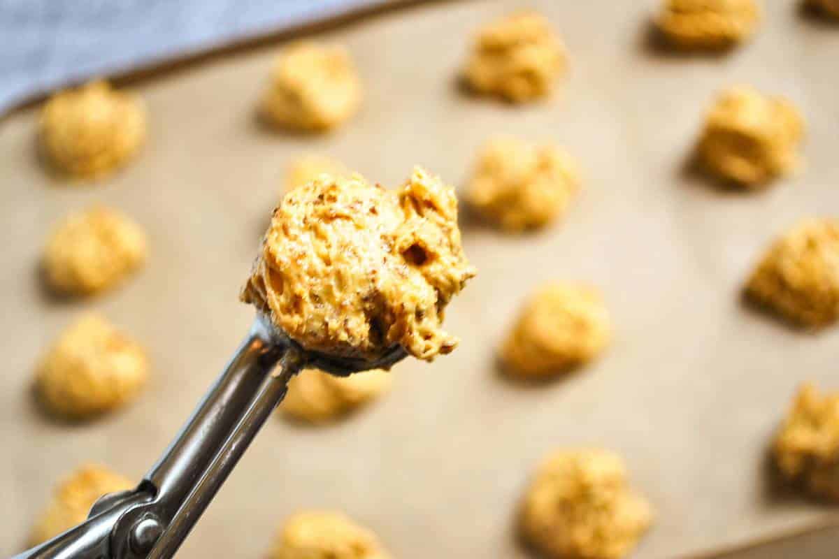 holding up a cookie scoop with batter over a baking sheet