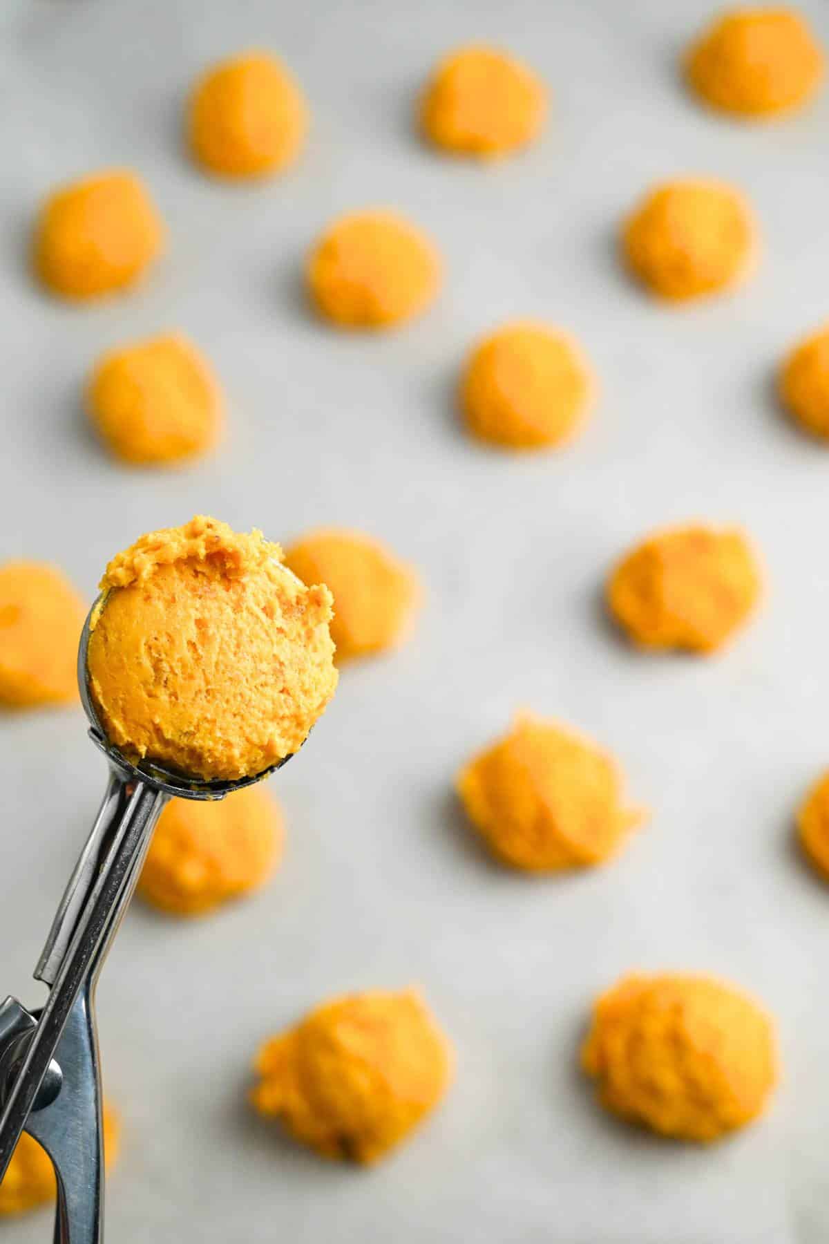 cookies on a baking sheet with a cookie scoop full of batter