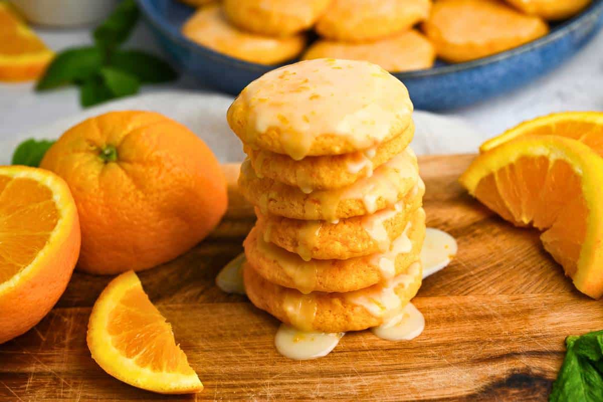 a stack of orange cookies with glaze and sliced oranges around it