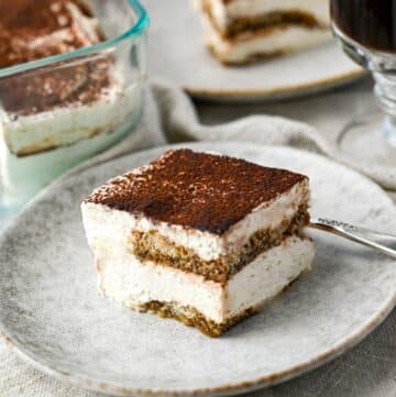 a slice of protein tiramisu on a plate with a serving behind it with a pan of tiramisu