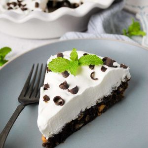 close up of a slice of chocolate pie with hazelnuts topped with cool whip, shaved chocolate and a fresh mint sprig